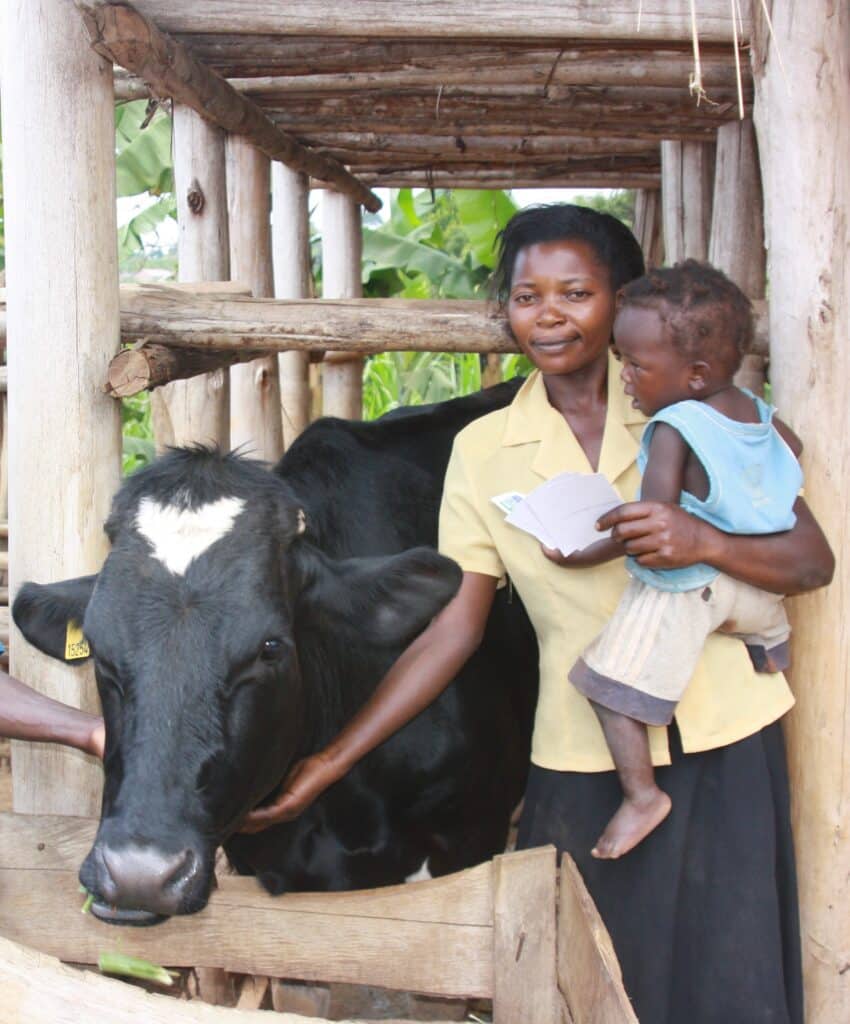 Matilda Namutebi holding her child and standing next to her cow.