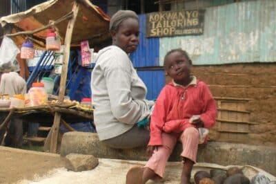 Woman sitting beside child and selling produce on the side of the road.