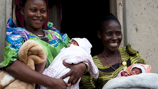 Two women smiling while they hold their babies.