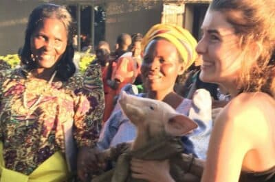 Group of people outside smiling around a woman holding a pig.