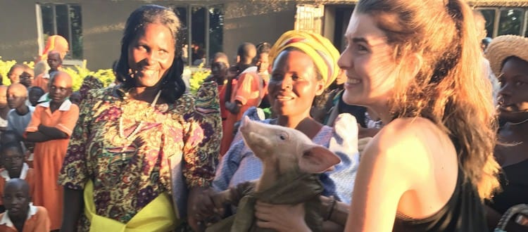 Group of people outside smiling around a woman holding a pig.
