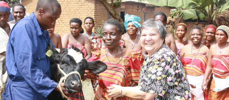 Group of people standing outside smiling around a cow.