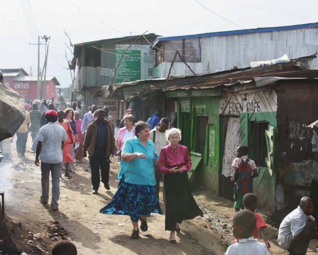 Group of people walking down a dirt road in an impoverished town.