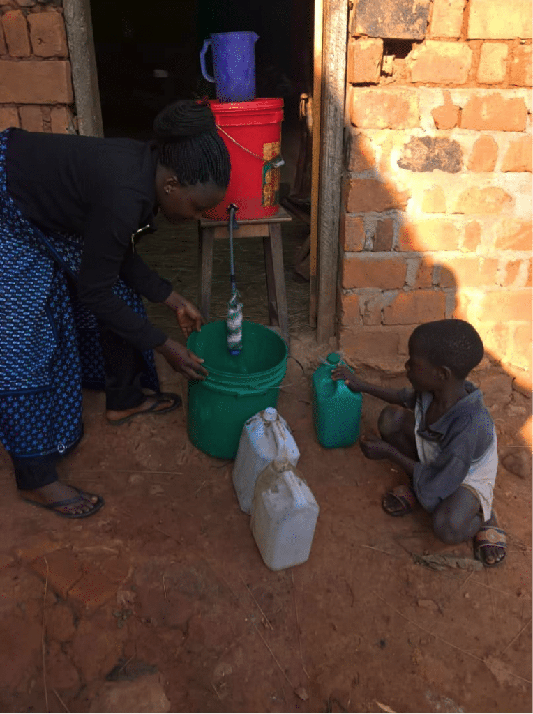 Woman and child filling a green bucket with filtered water.