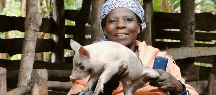 Woman smiling outside as she holds a piglet.