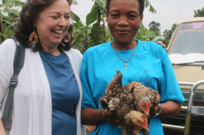 Two woman outside smiling as one holds two chickens.