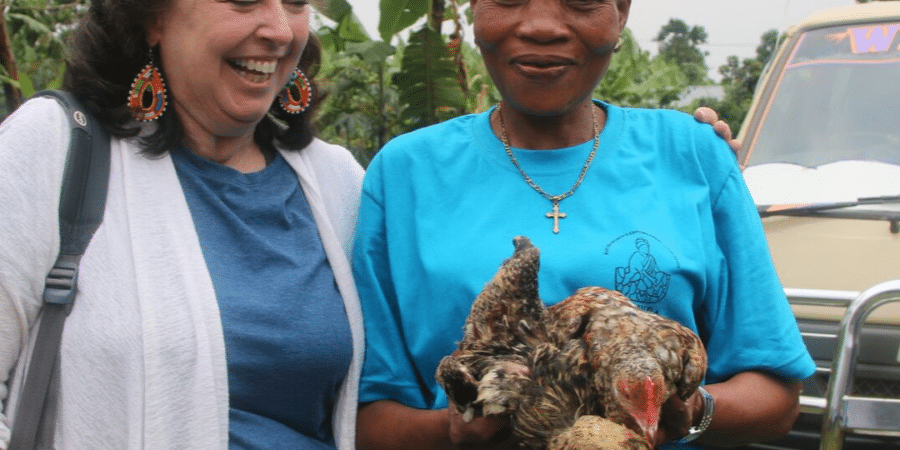 Two woman outside smiling as one holds two chickens.