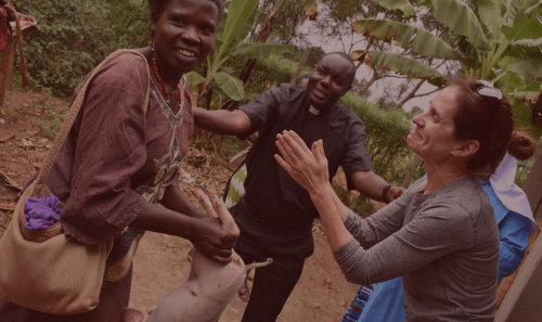 A woman outside is smiling as she receives a piglet from the small group of people with her.