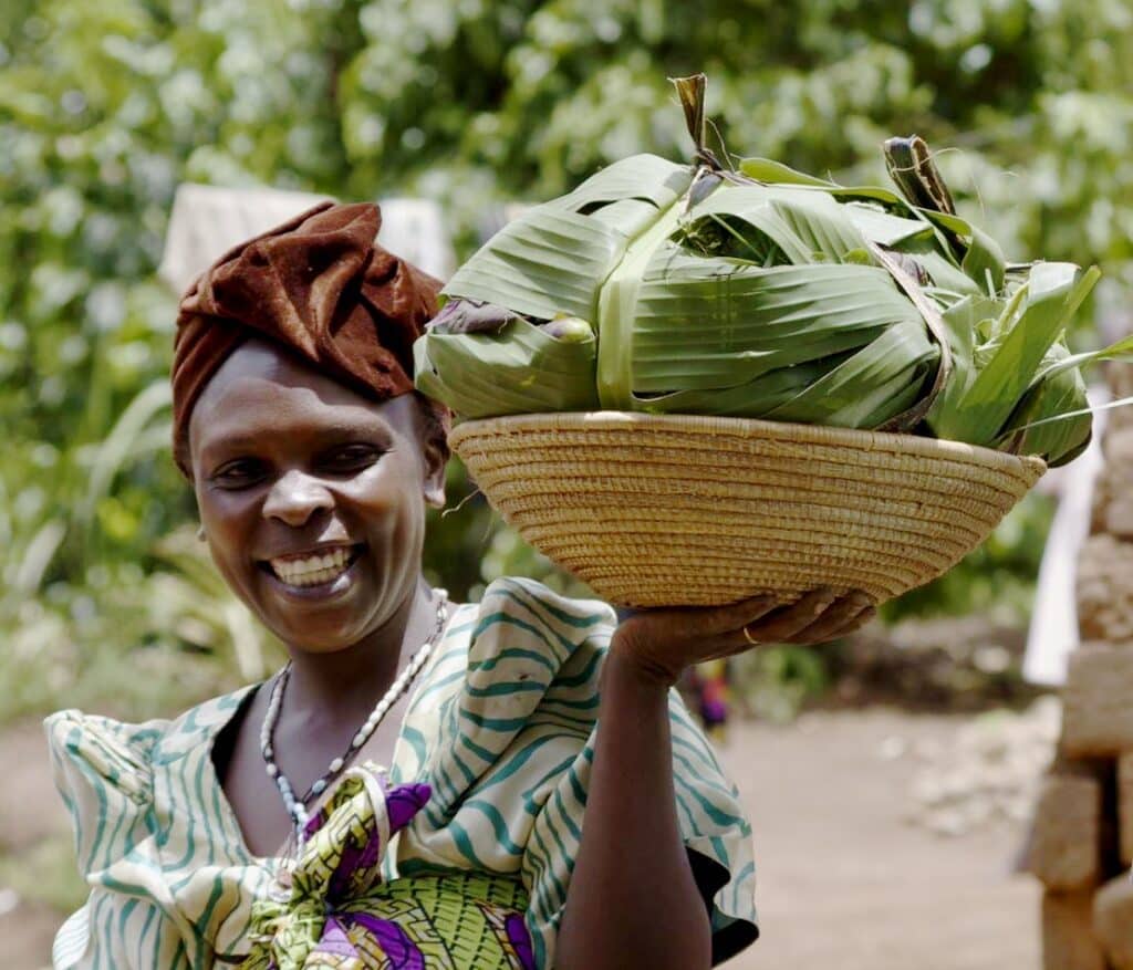 A woman outside smiling as she holds a basket of foodstuffs.