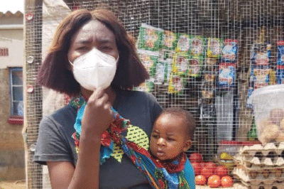 Woman wearing a face mask as she holds her baby outside.