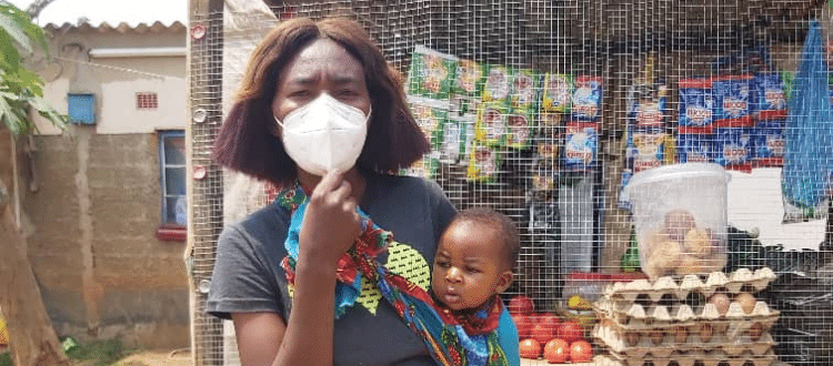 Woman wearing a face mask as she holds her baby outside.