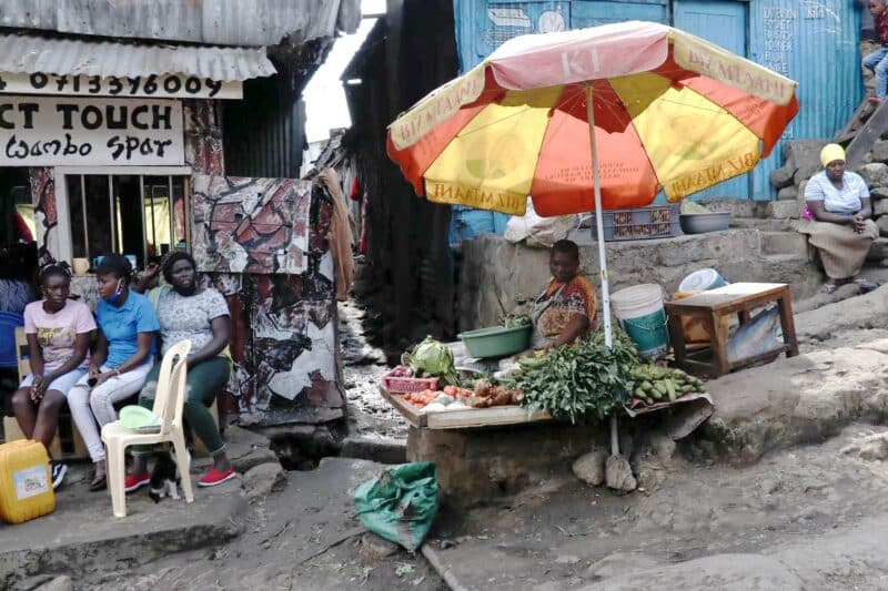 Woman selling produce at a vegetable stand with an umbrella.