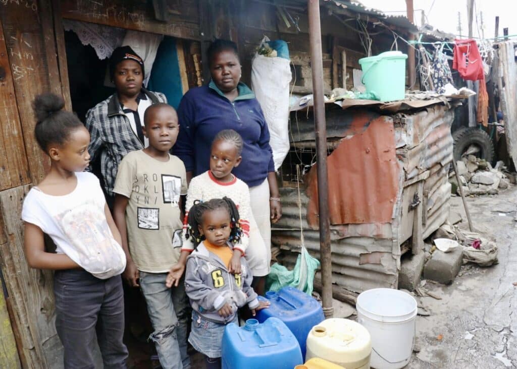 Woman and her children standing next to water jugs.