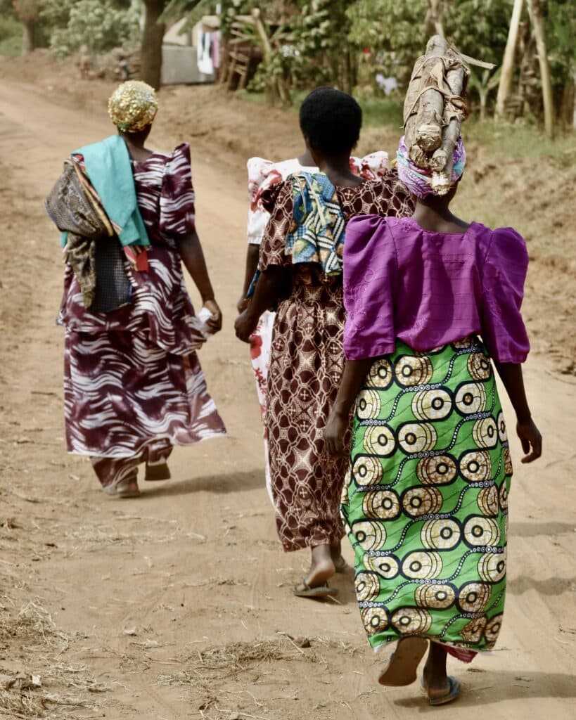 Three women walking on a dusty road.