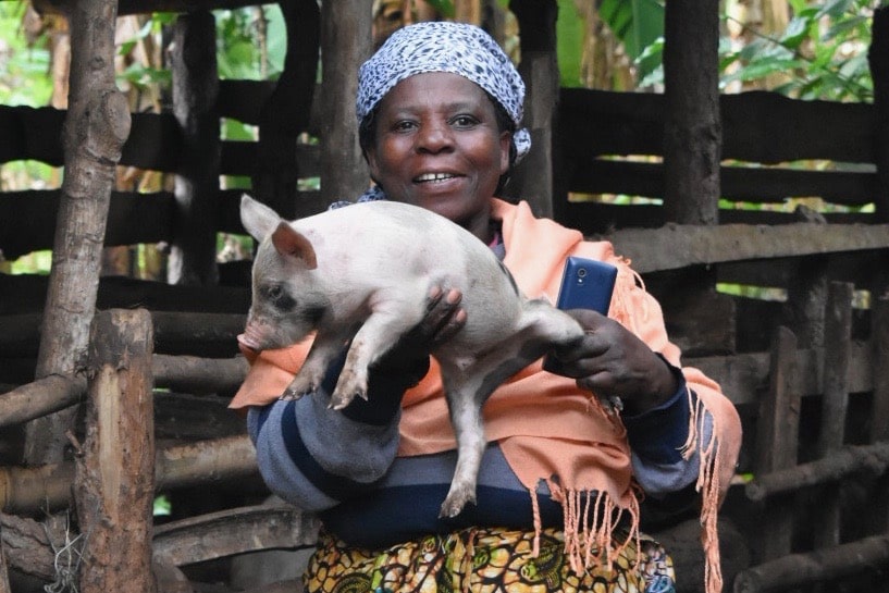 A woman smiling as she holds her piglet up.