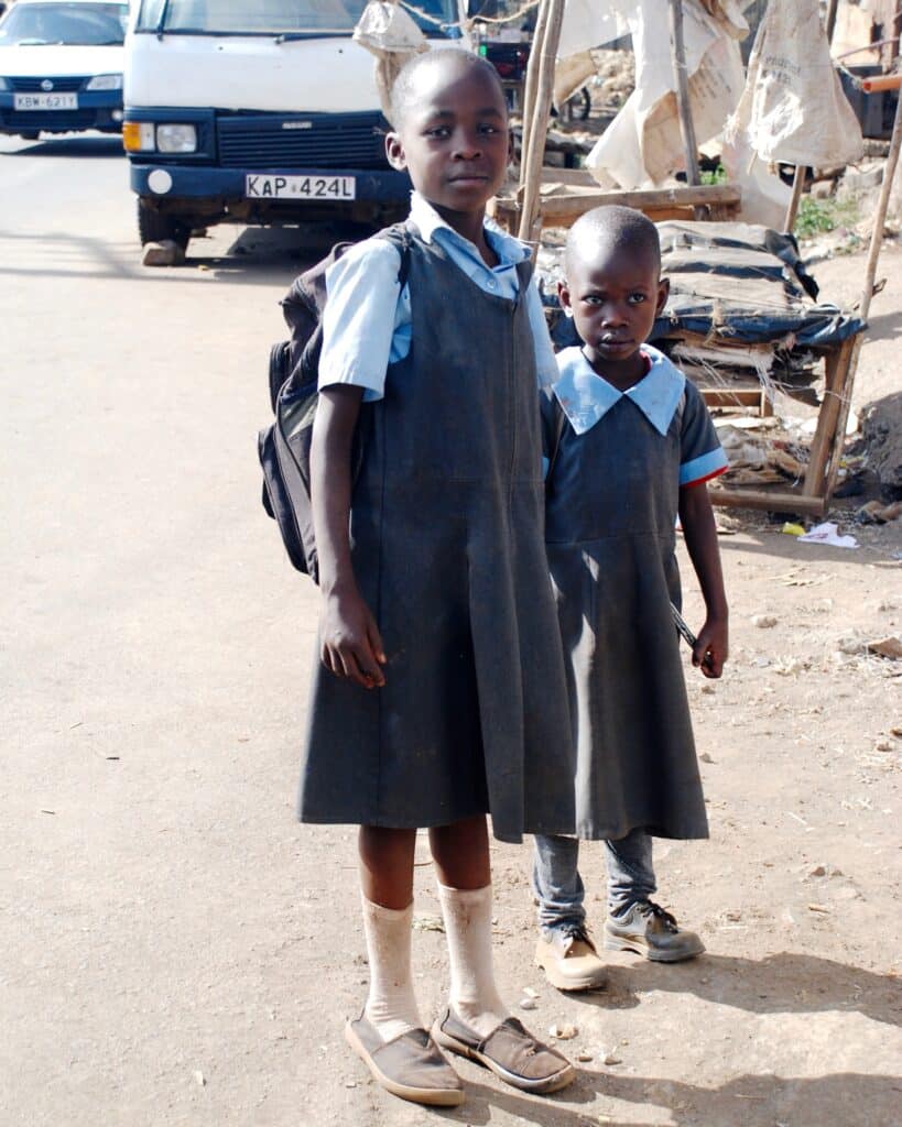 Two young children wearing school uniforms standing outside.