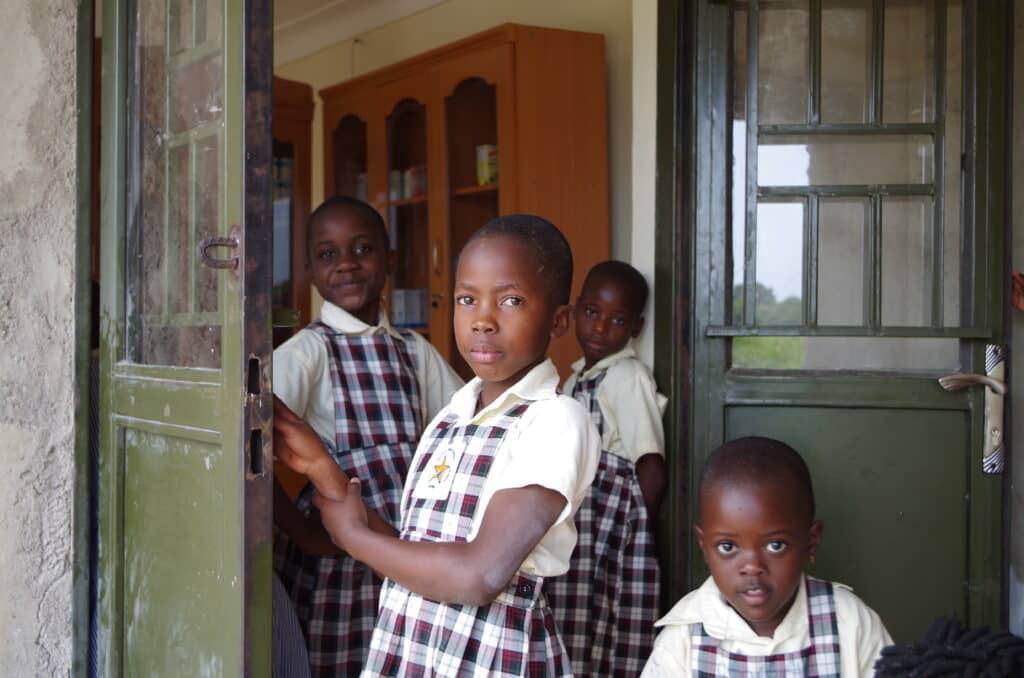 A small group of young children wearing school uniforms standing in a doorway.