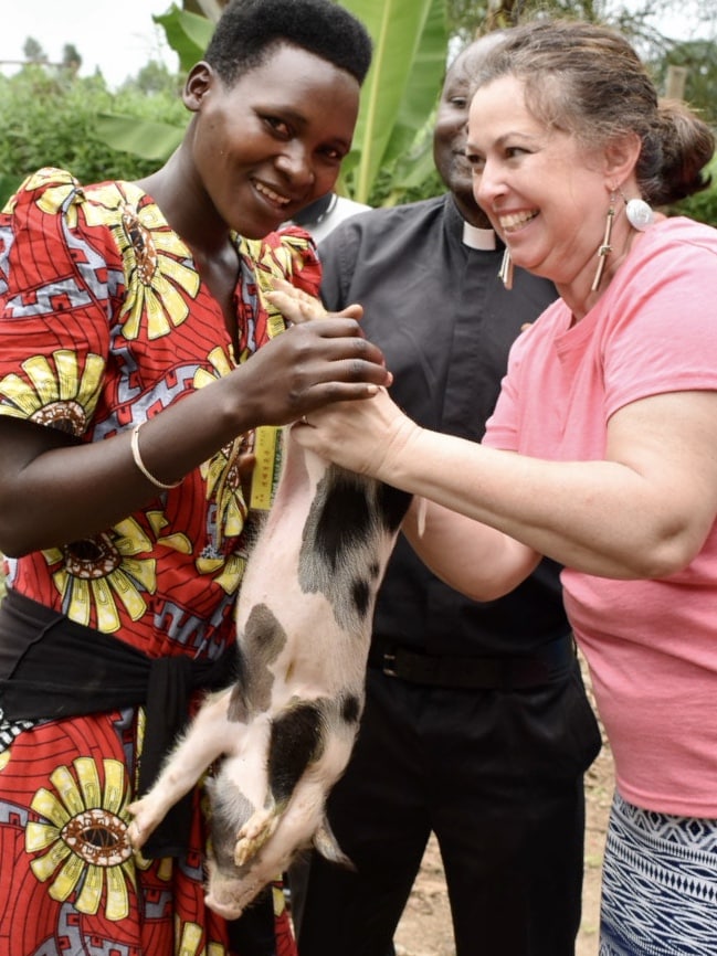 A woman handing a piglet to another woman.