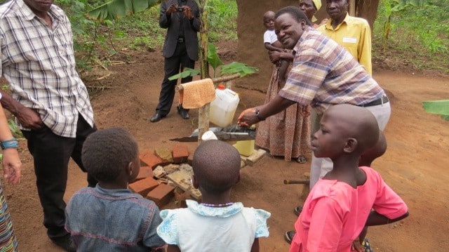 A man with a group of children outside using a tippy tap hand washing station.