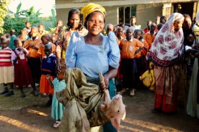 A woman smiling while she holds a piglet with a large group of people in the background.