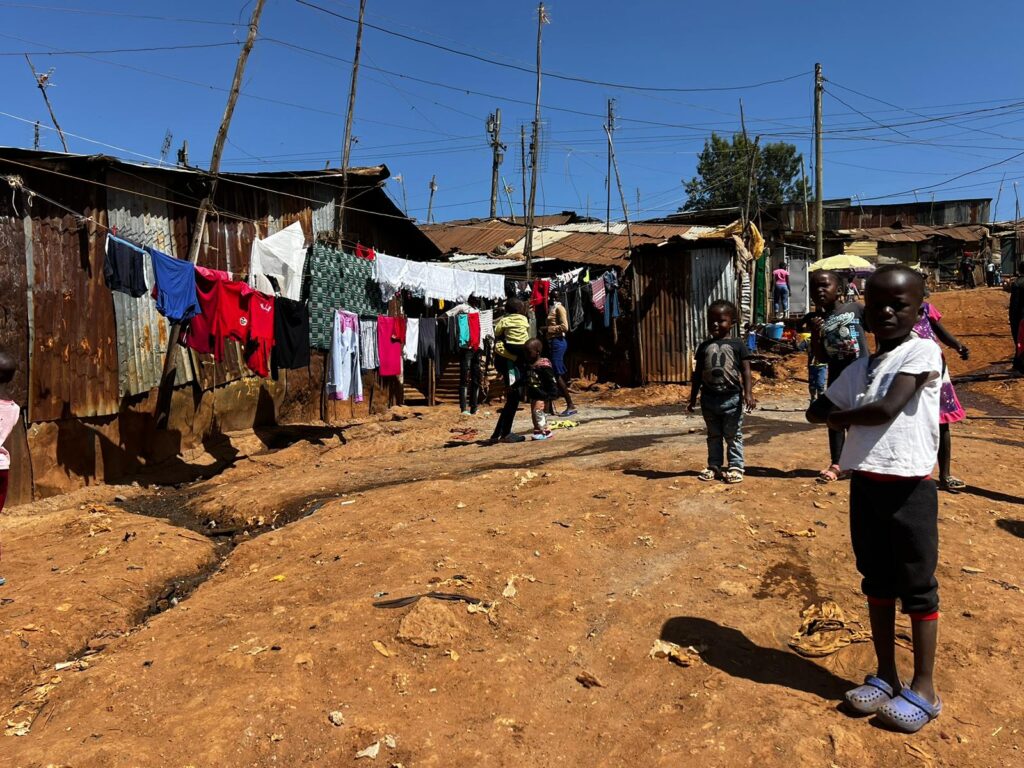 Young children standing on a dirt area with clothes drying on a line outside.