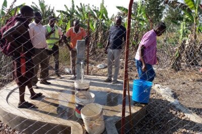 A group of men filling buckets of water from a community spigot.