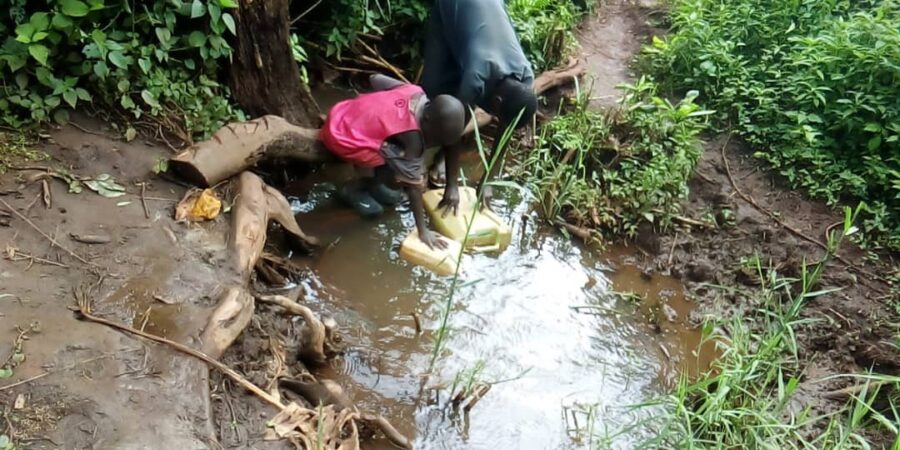 Two boys filling water jugs in small stream.