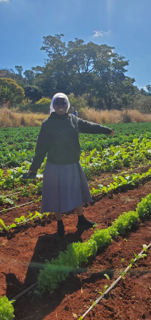 A woman smiling and pointing to crops growing in neat rows.