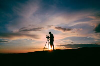 A man setting up a camera outside as the sun sets.