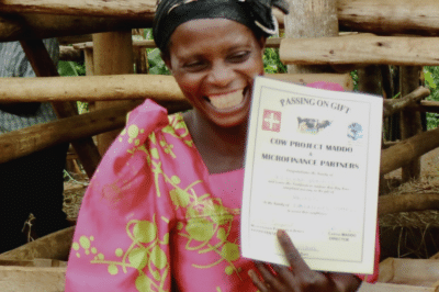 A woman smiling and holding up a document entitled: "Passing on gift. Cow Project Maddo & Microfinance Partners."